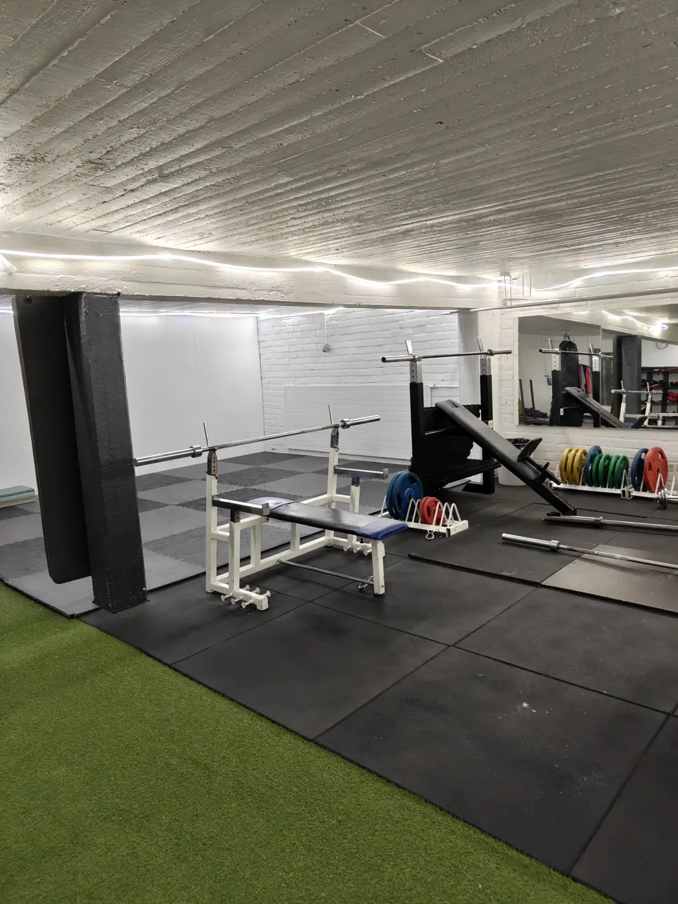 Bench press rack and barbell, with an artificial turf strip beside it