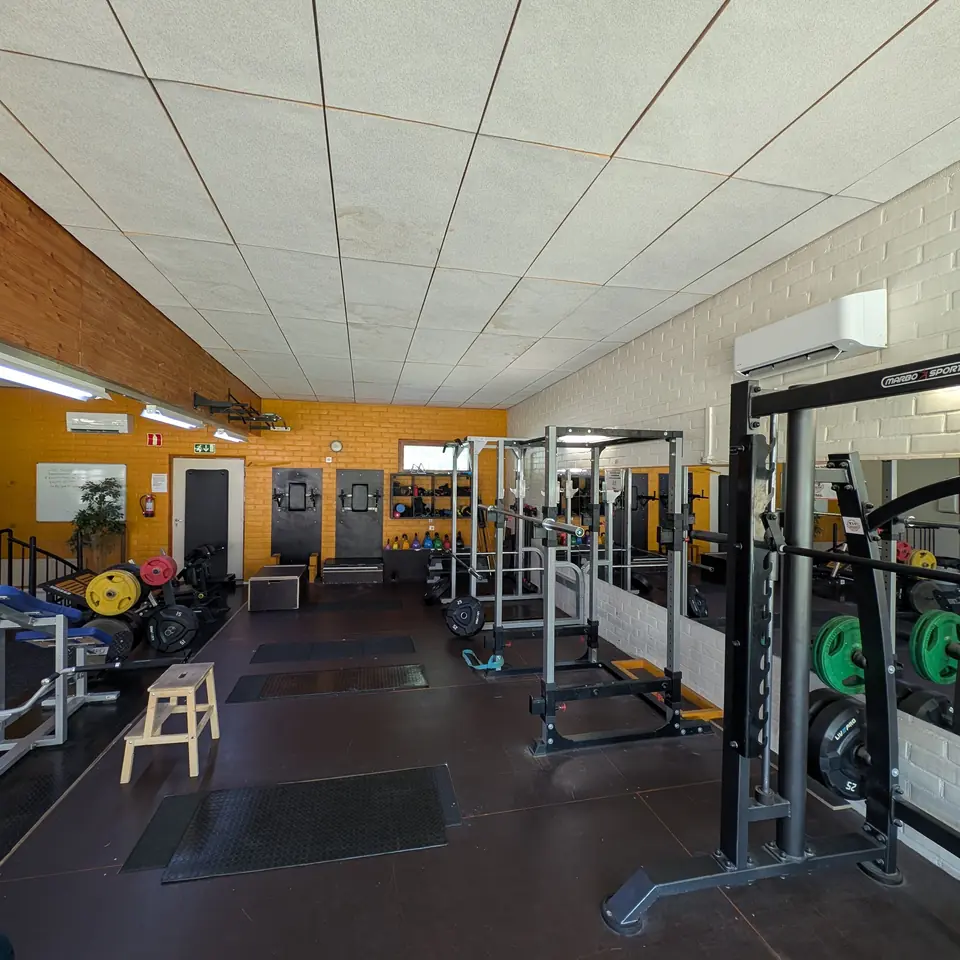 Free weights area: power racks, weight plates and kettlebells, with heat pumps on the ceiling