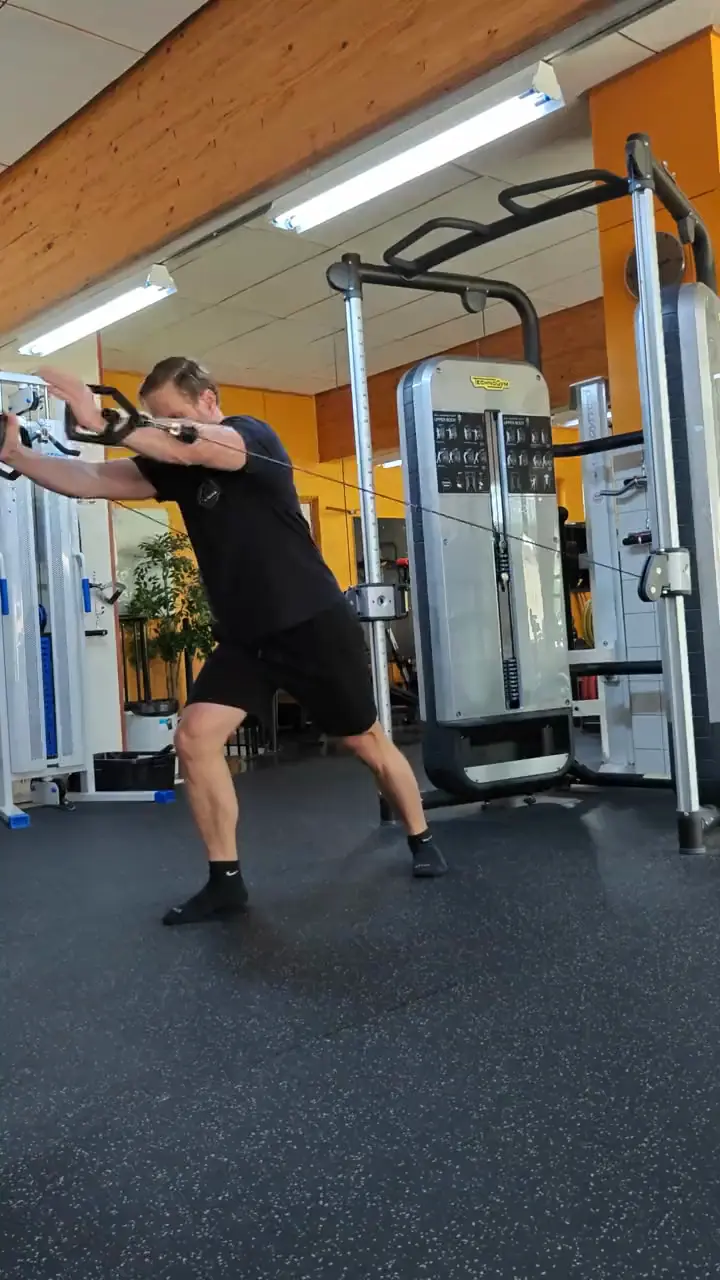 Joonas training on a cable machine with one arm, in front of an orange wall