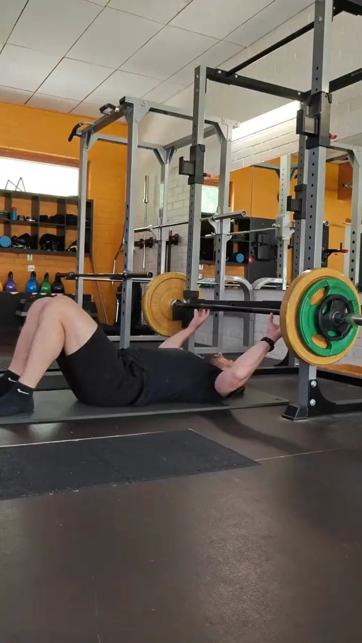 Joonas training: a floor press in the power rack in front of an orange brick wall