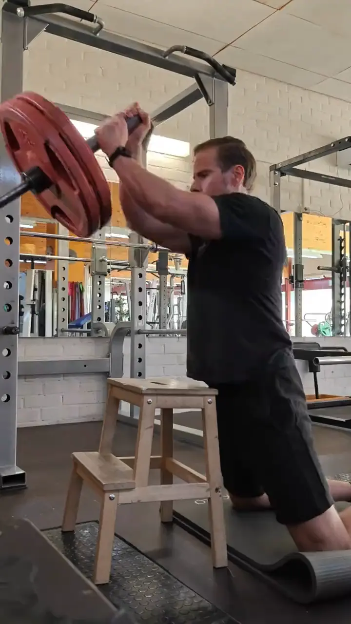 Joonas training: a barbell shoulder press from a kneeling position, red weight plates