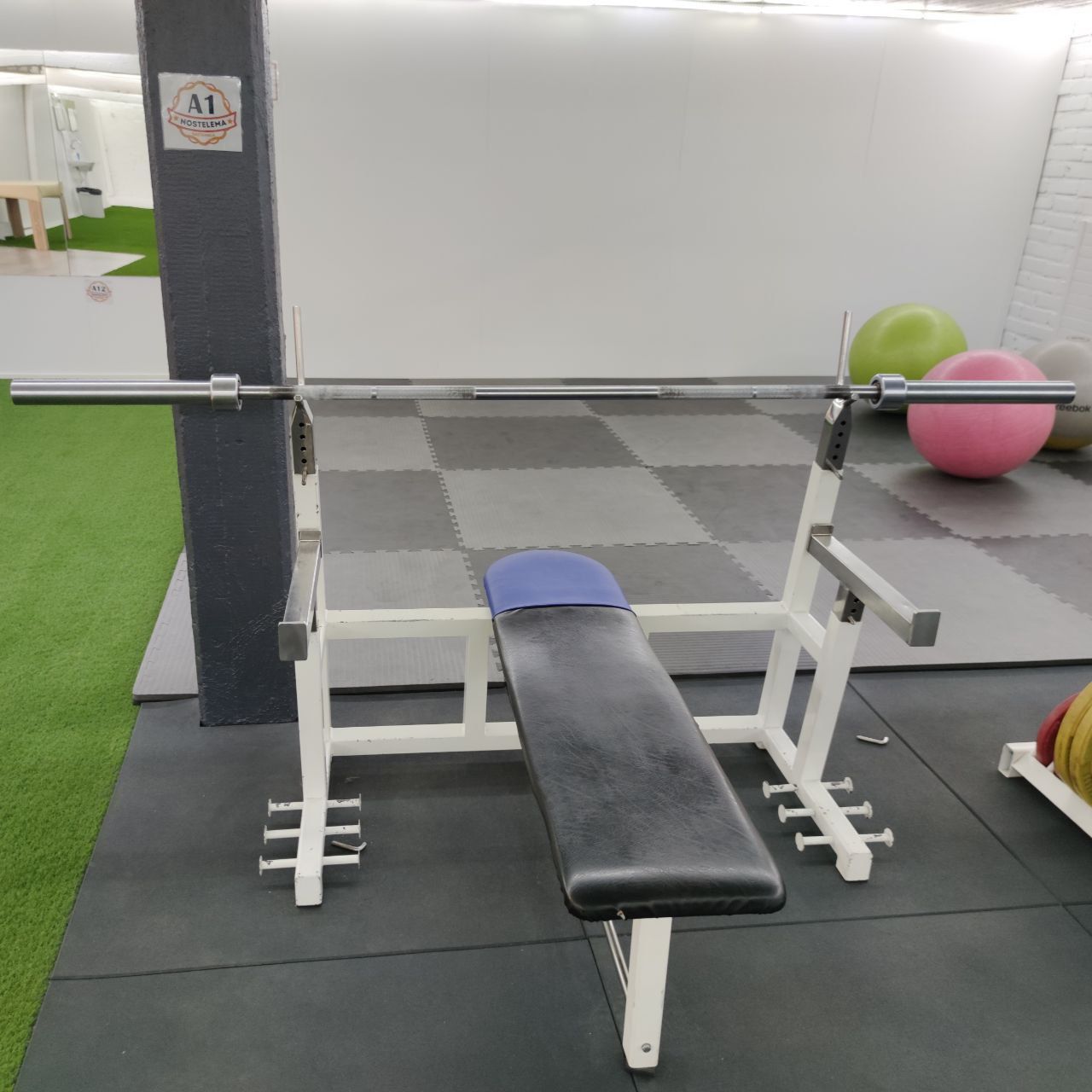 White-framed bench press rack with safety arms and a barbell with plates